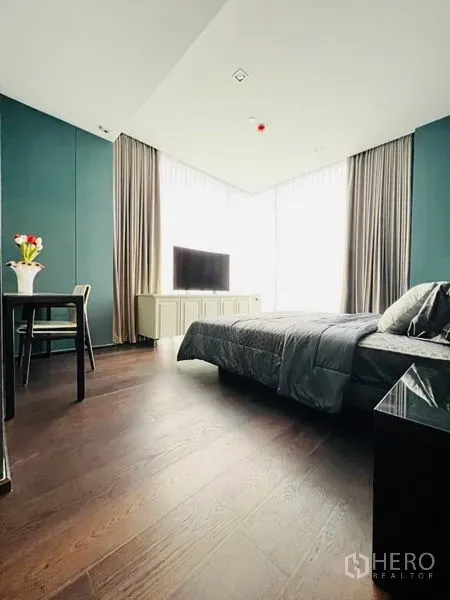 Condominium for rent in Watthana, Bangkok - Primary bedroom angle showing tall corner windows with sheer curtains and a TV console.