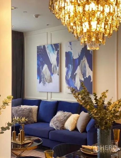 公寓 出租 - 从餐区望向客厅，蓝色转角沙发、吊灯与抽象装饰画。