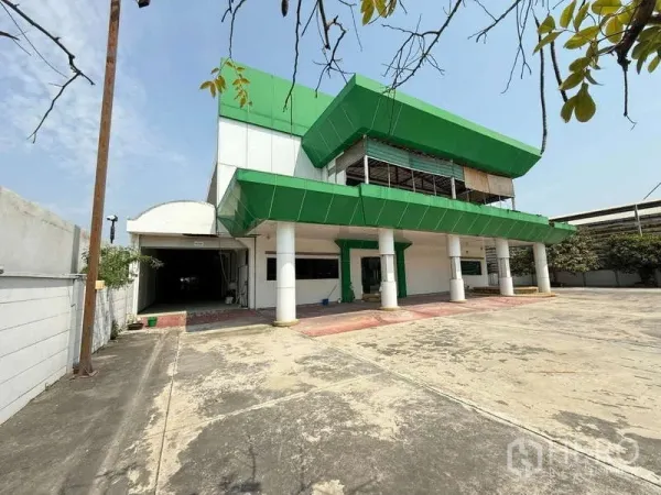 货栈 出租在Mueang Samut Prakan, Samut Prakan - 绿白色两层办公楼外观，前方配超大混凝土场地与停车区。