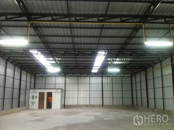 Warehouse for rent in Wang Thonglang, Bangkok - Open warehouse hall with corrugated metal walls, skylight panels, bright lighting, and a small internal office room.