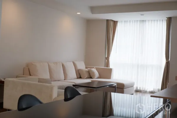 คอนโด ให้เช่าในPathum Wan, Bangkok - ห้องนั่งเล่นอบอุ่น โซฟามุมสีครีม โต๊ะกลาง และหน้าต่างมุมห้องพร้อมม่านโปร่ง