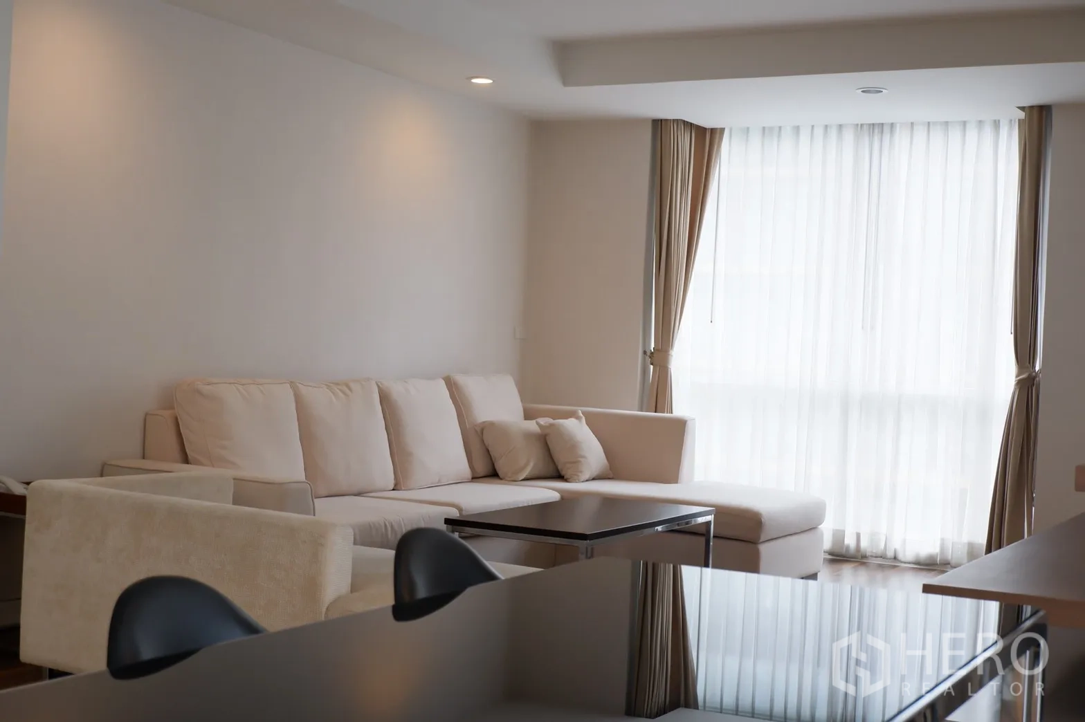 คอนโด ให้เช่าในPathum Wan, Bangkok - ห้องนั่งเล่นอบอุ่น โซฟามุมสีครีม โต๊ะกลาง และหน้าต่างมุมห้องพร้อมม่านโปร่ง