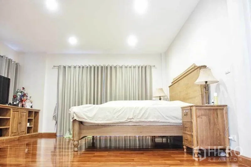 独立式住宅 出租或出售在Pak Kret, Nonthaburi - 宽敞主卧，木质床、床头柜、木地板与嵌灯。