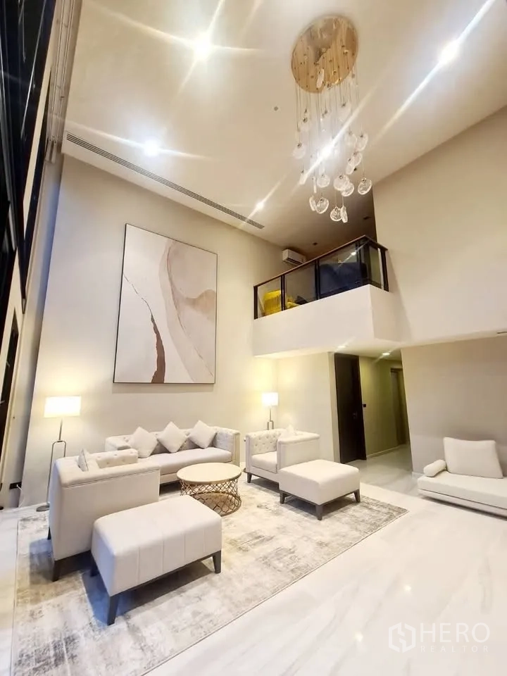 Townhouse for rent or sale in Watthana, Bangkok - Double-height living room with chandelier, sofas, and mezzanine above.