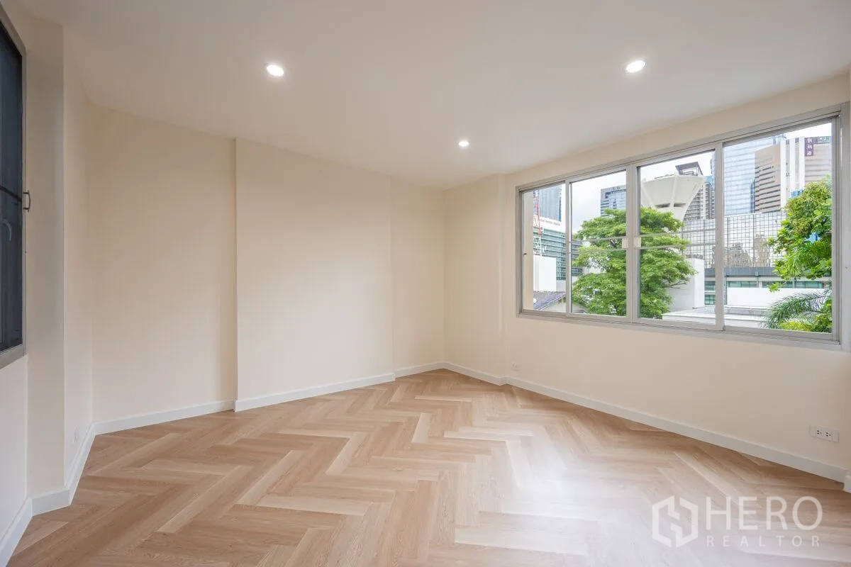 Detached House for rent or sale in Chatuchak, Bangkok - Sunlit bedroom with herringbone floor and wide windows overlooking greenery and city.