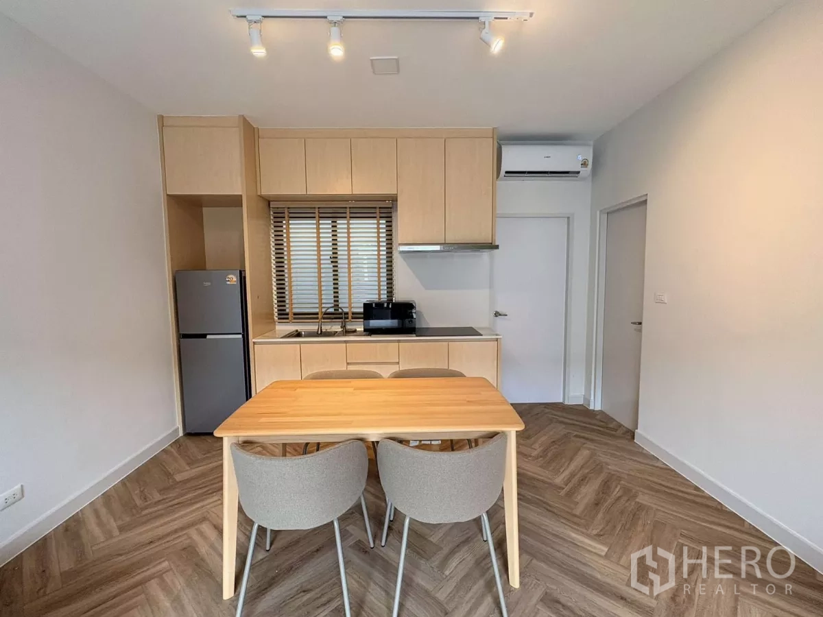 Townhouse for rent in Bang Phli, Samut Prakan - Compact built-in kitchen with cabinets, cooktop, refrigerator and a wooden dining table.