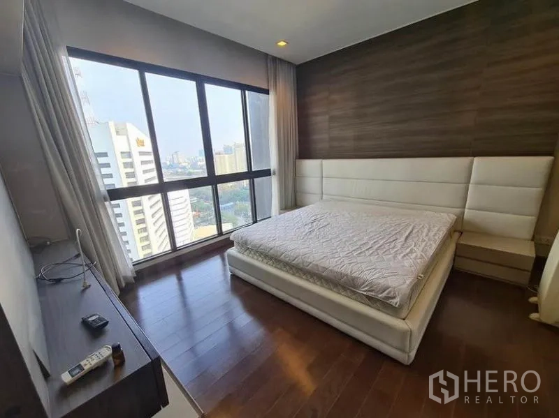 Condominium for rent or sale in Huai Khwang, Bangkok - Spacious master bedroom with feature wall, king bed and wide city-facing windows.