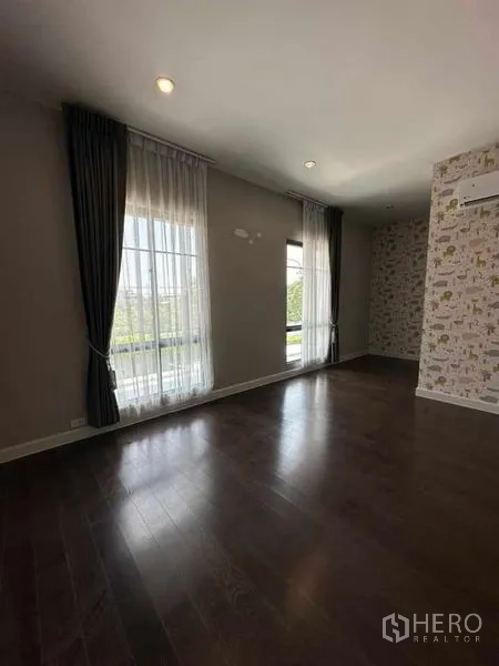 Detached House for sale in Prawet, Bangkok - Sunlit bedroom with dark wood floor, large windows and a patterned accent wall.