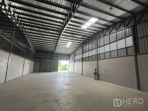 Warehouse for rent in Bang Bua Thong, Nonthaburi - Open-plan storage area with ventilated metal walls and a large rear door bringing in daylight.