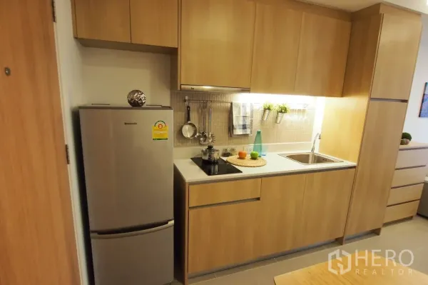 Condominium for rent in Pathum Wan, Bangkok - Compact modern kitchen with wood cabinets, electric hob, sink and full-size fridge.