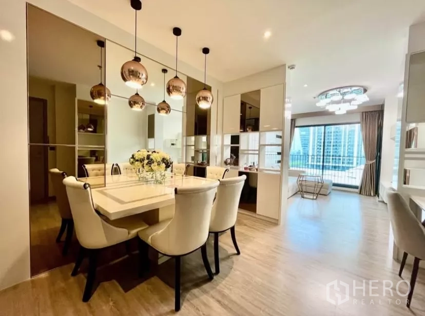 คอนโด ให้เช่าในWatthana, Bangkok - พื้นที่รับประทานอาหารหรู ผนังกระจก โคมไฟห้อย และโต๊ะ 6 ที่นั่ง เชื่อมสู่ห้องนั่งเล่นและระเบียงวิวเมือง