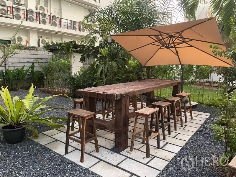 พื้นที่ขายปลีก ให้เช่าในSuan Luang, Bangkok - โต๊ะไม้ยาวพร้อมสตูลใต้ร่มขนาดใหญ่ ข้างสวนสีเขียว