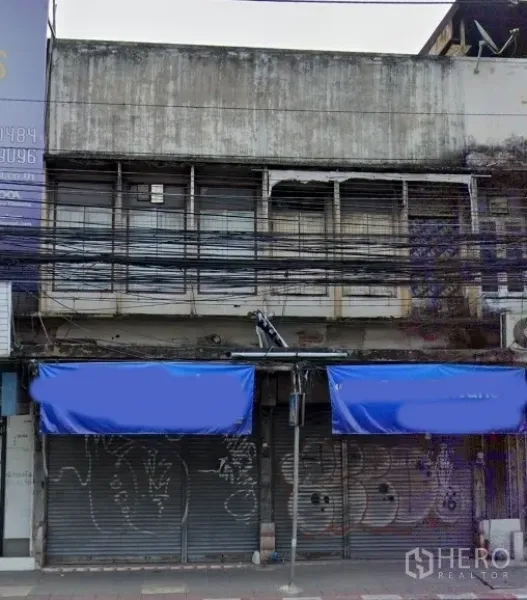 店屋 出售在Watthana, Bangkok - 临街商铺外立面，蓝色雨棚与金属卷闸门，上层为带护栏窗户，位于曼谷瓦塔纳区。