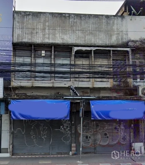 店屋 出售在Watthana, Bangkok - 临街商铺外立面，蓝色雨棚与金属卷闸门，上层为带护栏窗户，位于曼谷瓦塔纳区。