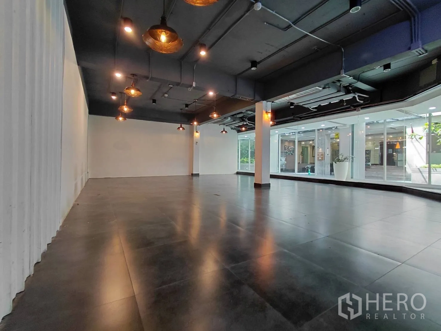 零售空间 for rent in Ratchathewi, Bangkok - 开放式室内空间，深色地砖、裸露天花与吊灯，大面积玻璃橱窗。