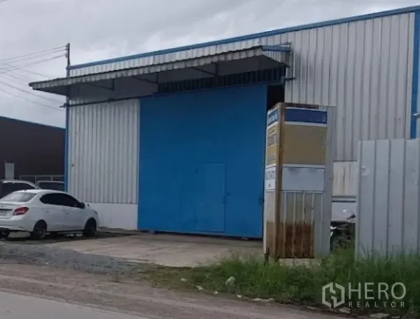 Warehouse for rent in Min Buri, Bangkok - Street-facing warehouse in Min Buri with a large blue steel sliding door, metal cladding, covered loading bay and concrete driveway.
