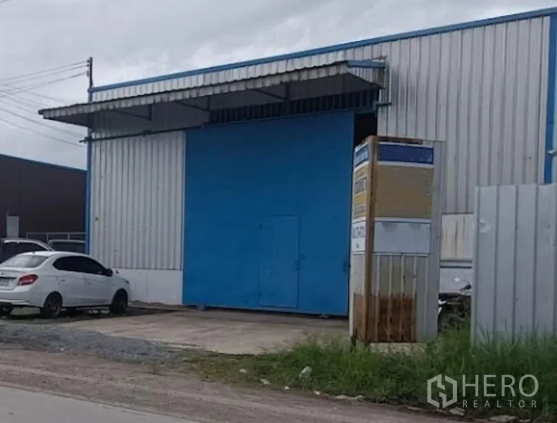Warehouse for rent in Min Buri, Bangkok - Street-facing warehouse in Min Buri with a large blue steel sliding door, metal cladding, covered loading bay and concrete driveway.