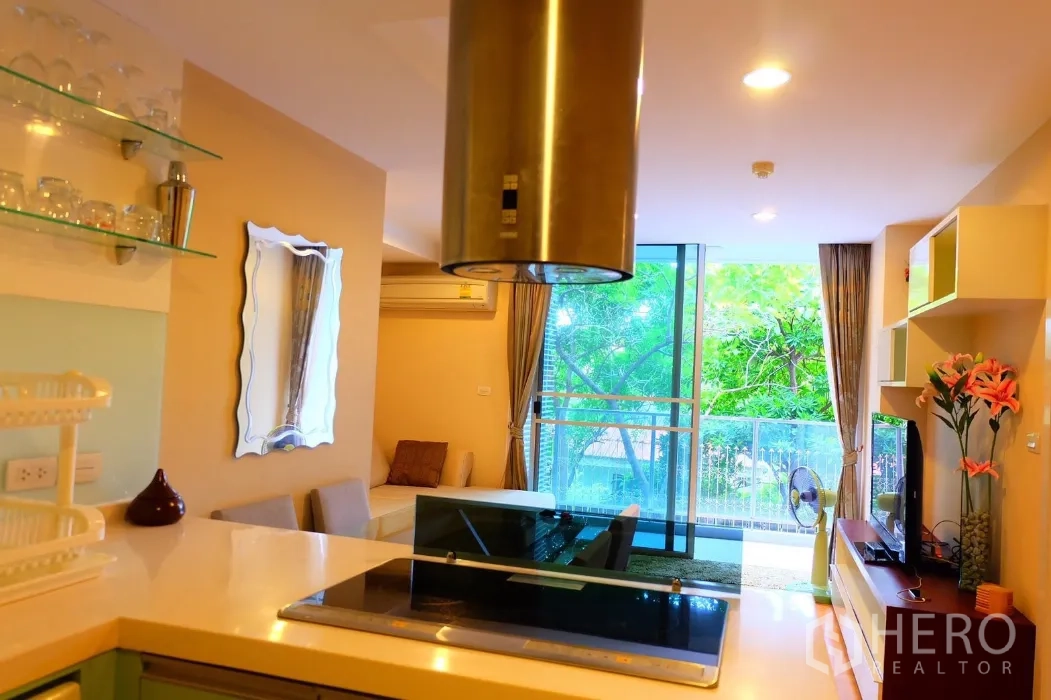 คอนโด ให้เช่าในPhaya Thai, Bangkok - มุมมองจากครัวสู่ห้องนั่งเล่นและระเบียง พร้อมประตูกระจกบานเลื่อนและวิวต้นไม้