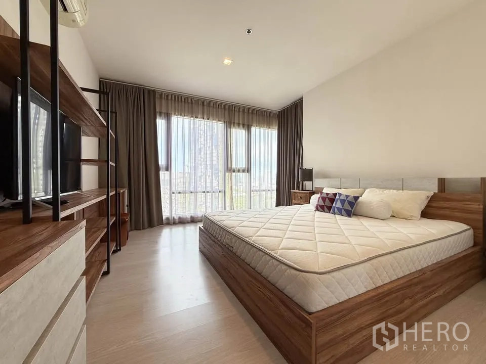 Condominium for rent in Khlong Toei, Bangkok - Airy room with expansive windows, bedside tables and city skyline beyond.
