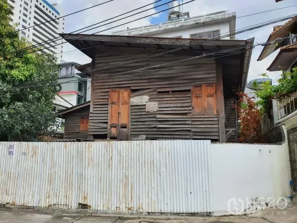 Detached House for rent in Sathon, Bangkok - Street view of an aged wooden house behind a white corrugated fence in urban Bangkok.