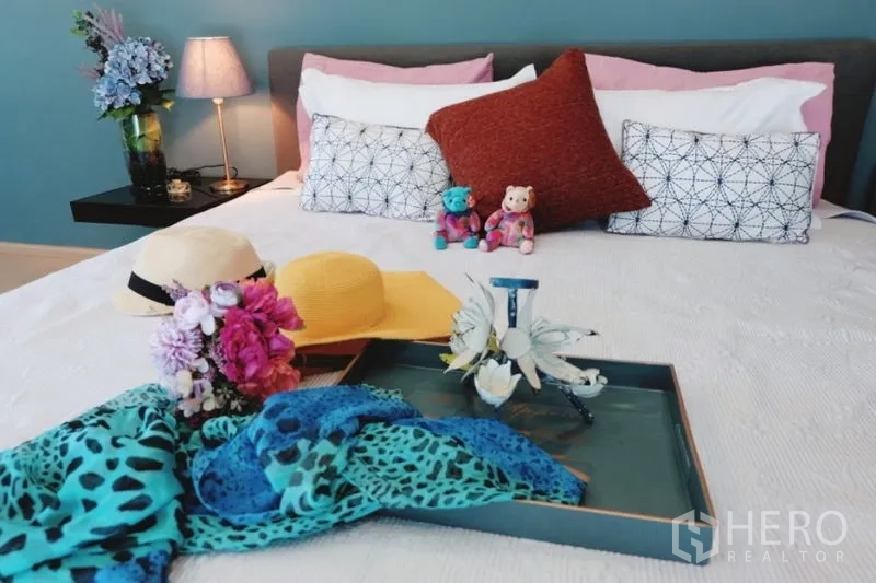 Townhouse for rent in Khlong Toei, Bangkok - Styled bedroom bed with colorful pillows, tray and accessories against a teal wall.