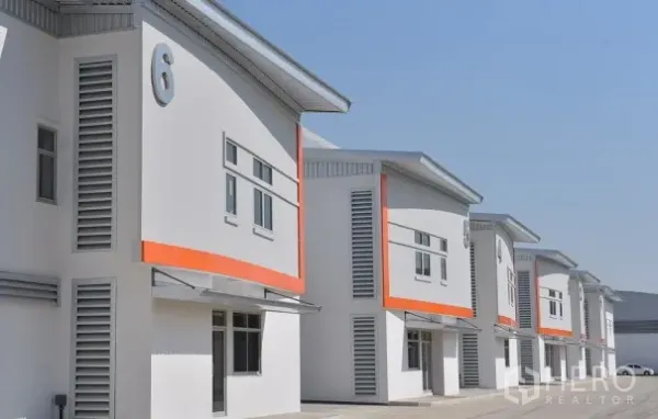 工厂 出租在Phra Nakhon Si Ayutthaya - 安保园区内的现代化厂房外立面，编号立面与橙色装饰，车道宽阔。