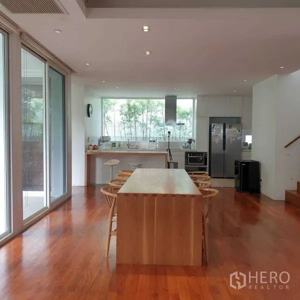 Detached House for rent in Watthana, Bangkok - Bright open-plan kitchen with large wooden island, dining chairs, stainless appliances and sliding glass doors over warm wood floors.
