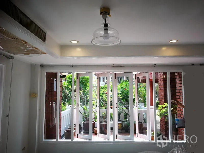 Townhouse for rent or sale in Watthana, Bangkok - Bright room with wall-to-wall windows opening to a green balcony terrace.