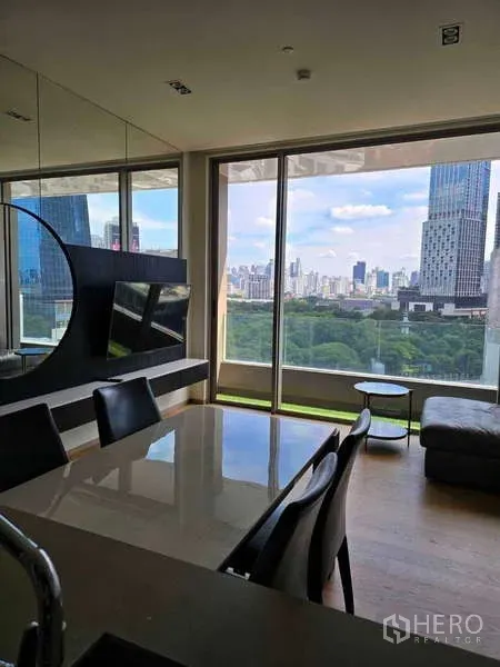 公寓 出租或出售在Bang Rak, Bangkok - 餐区带镜面墙与电视柜，旁为全景窗户与公园景观。