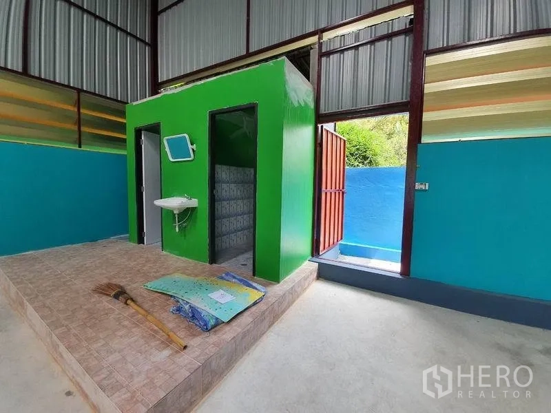 Warehouse for rent in Nonthaburi - Raised green restroom block with two doorways, a wall-mounted sink and tiled platform inside the warehouse near a side exit.