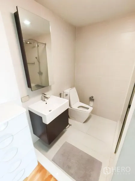 คอนโด ให้เช่าในKhlong Toei, Bangkok - ห้องน้ำสว่างพร้อมอ่างล้างหน้าแขวนผนัง กระจกเงา และโถสุขภัณฑ์บนพื้นกระเบื้องสีอ่อน