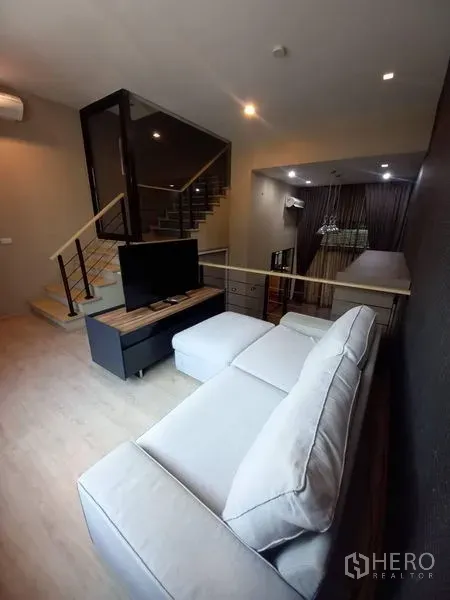 Townhouse for rent in Suan Luang, Bangkok - Open-plan lounge with sectional sofa facing TV and dining area beside the staircase.