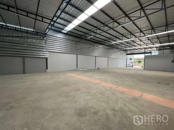 Warehouse for rent in Krathum Baen, Samut Sakhon - Open clear‑span warehouse floor with metal cladding walls, roof lighting strips and a roller‑shutter entrance.