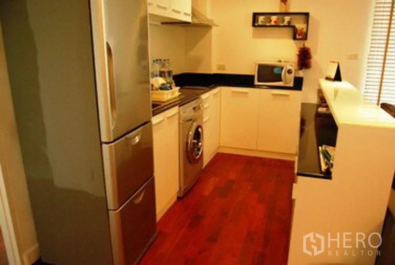 公寓 出租在Pathum Wan, Bangkok - U 形厨房，配不锈钢冰箱、洗衣机、白色柜体与深色台面。