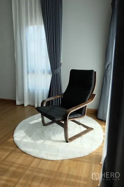 Detached House for rent in Bang Phli, Samut Prakan - Cozy reading corner with black lounge chair on a round rug beside tall curtains.