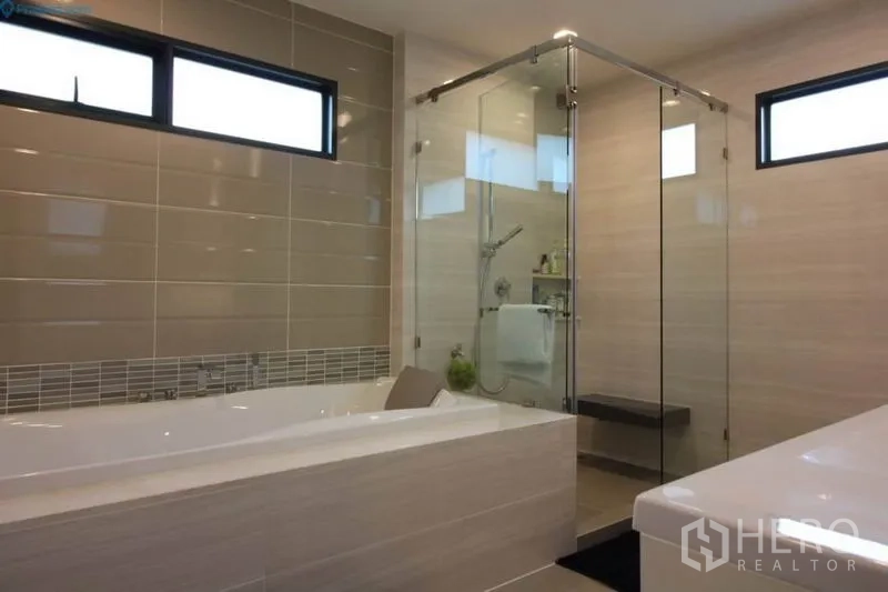 Detached House for rent or sale in Prawet, Bangkok - Contemporary bathroom featuring a soaking bathtub, glass-enclosed shower, and horizontal windows.