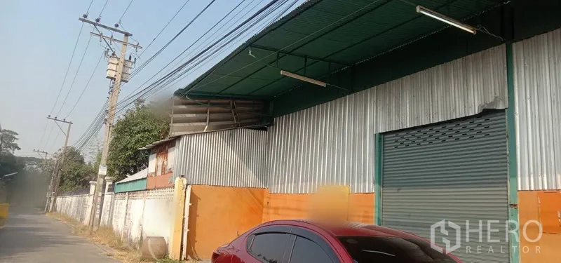 คลังสินค้า ให้เช่าในBueng Kum, Bangkok - ด้านหน้าโกดังติดถนน ผนังเมทัลชีท กันสาดสีเขียว พร้อมประตูม้วนขนาดใหญ่ ในเขตบึงกุ่ม กรุงเทพฯ