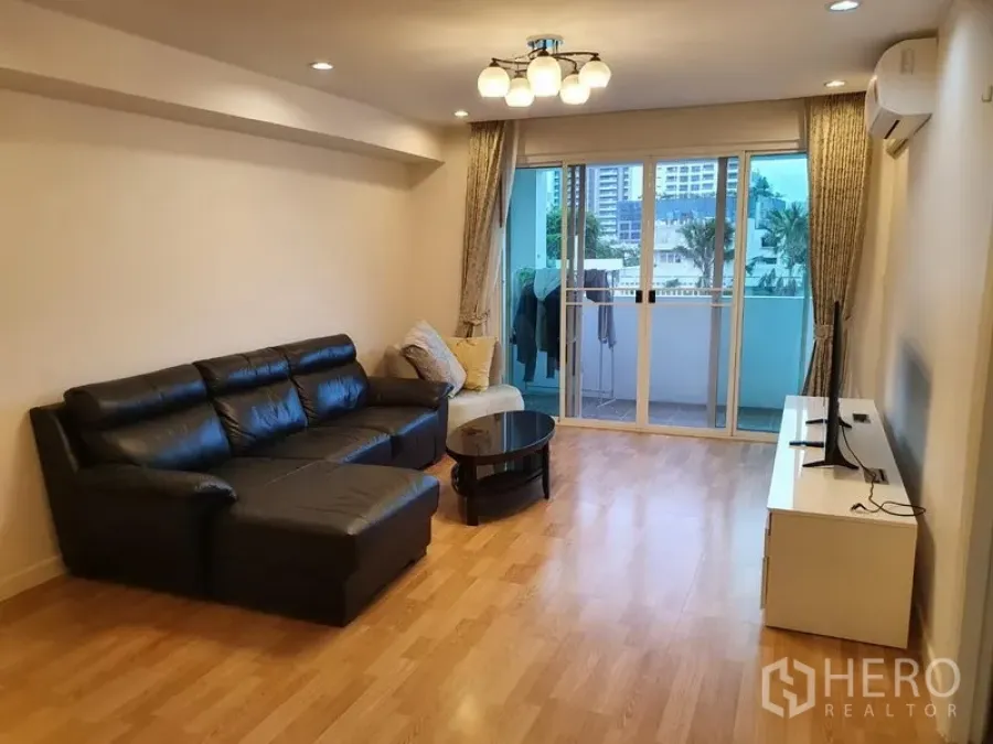 Condominium for rent in Watthana, Bangkok - Spacious living room with black leather sectional sofa, TV stand, and sliding doors to a balcony.