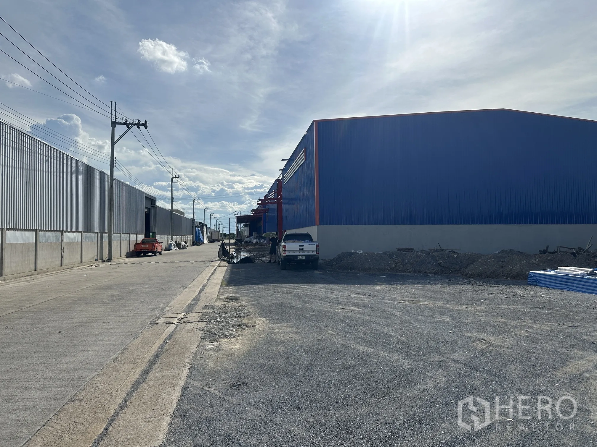Land for sale in Sai Noi, Nonthaburi - Wide concrete access road with power poles beside large warehouse buildings.