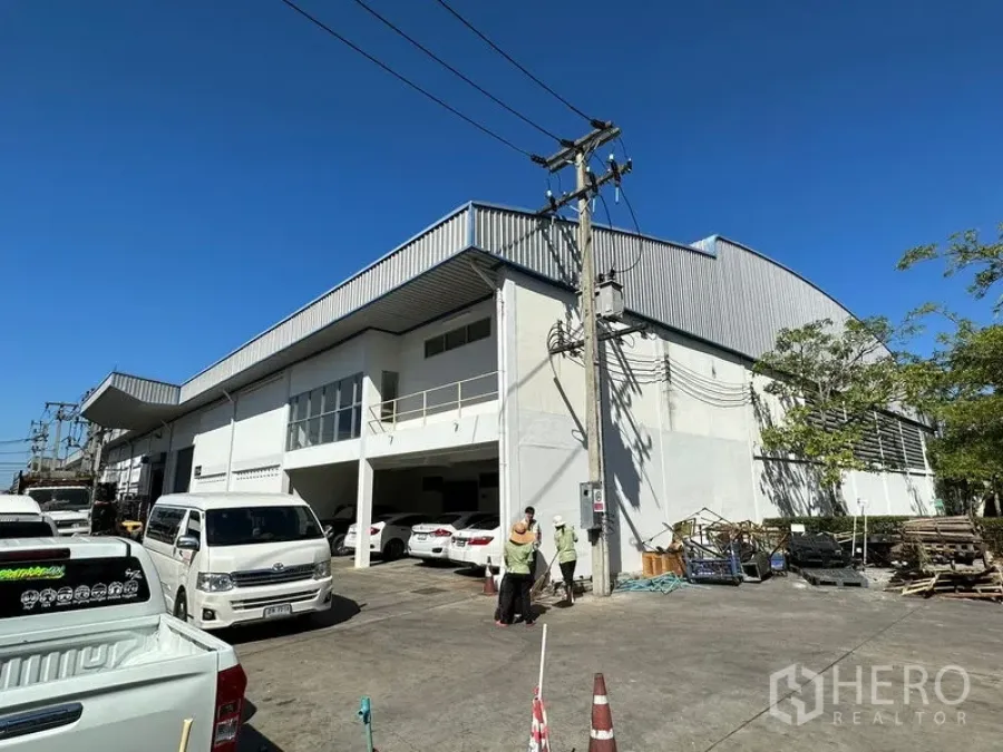 工厂 出租在Si Racha, Chon Buri - 春武里是拉差现代白色工厂外观，金属屋顶，室外停车位与电线杆，蓝天之下。