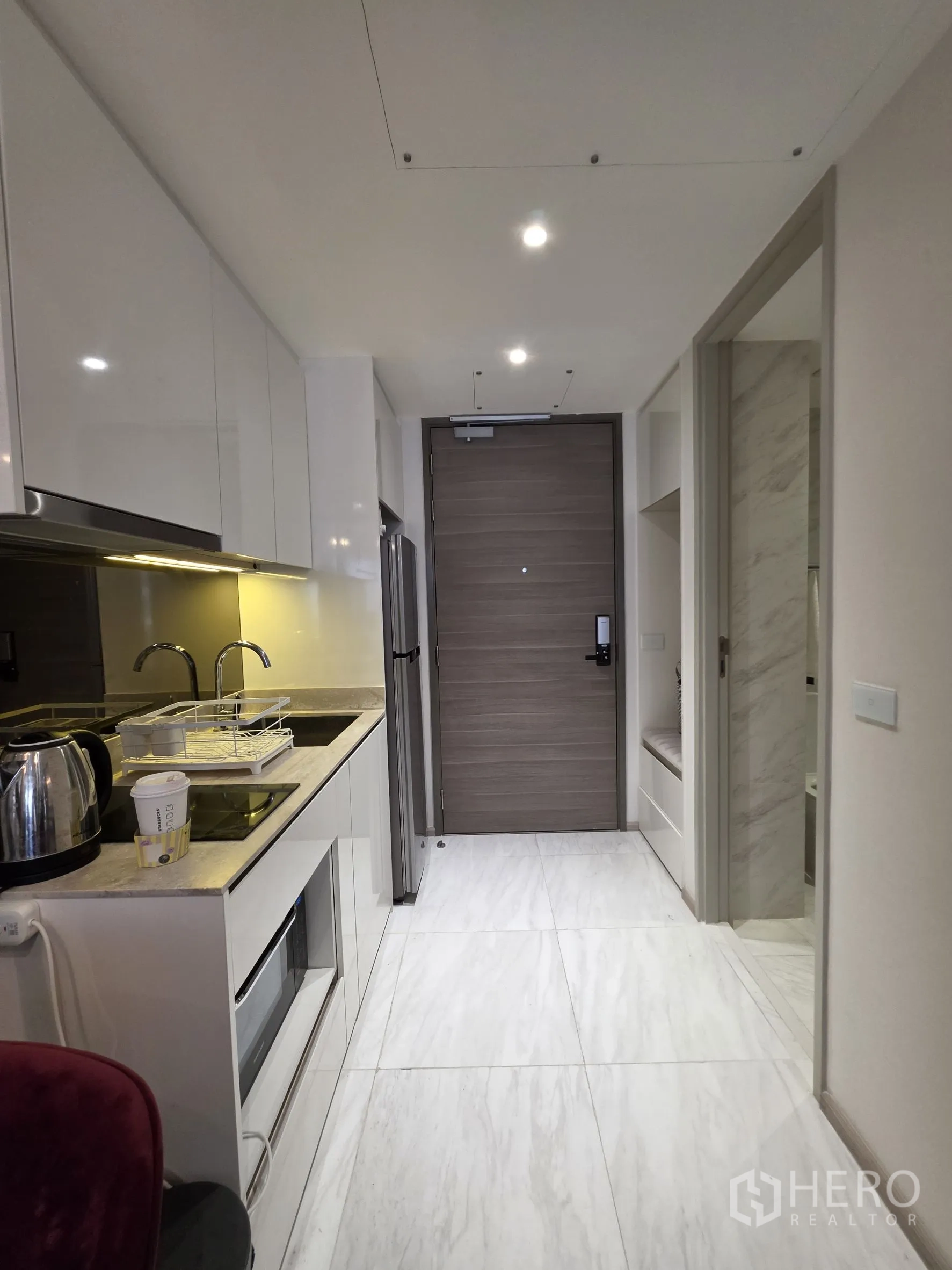 คอนโด for rent in Khlong Toei, Bangkok - ครัวแบบแกลเลอรี่ตู้สีขาวยาวไปถึงประตูทางเข้า ด้านขวามีประตูห้องน้ำ