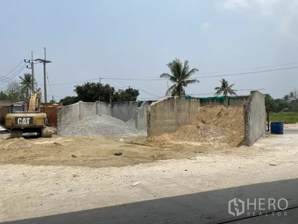 工厂 出售在Chon Buri - 院内空地配挖掘机，砂石料储区，周边可见棕榈树与绿化。