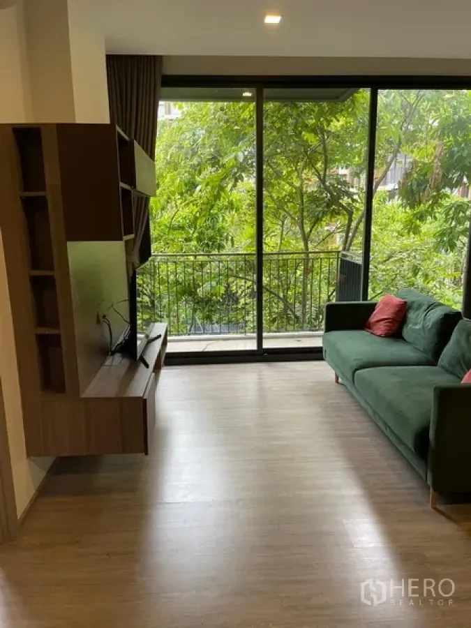 Condominium for rent in Watthana, Bangkok - Bright lounge facing large sliding glass doors to a balcony overlooking lush trees.