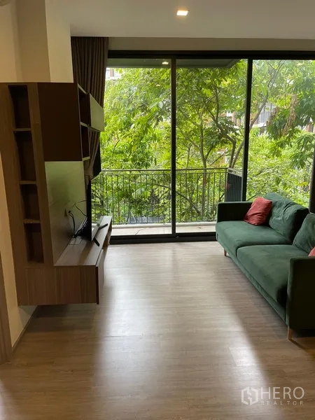 Condominium for rent in Watthana, Bangkok - Bright lounge facing large sliding glass doors to a balcony overlooking lush trees.