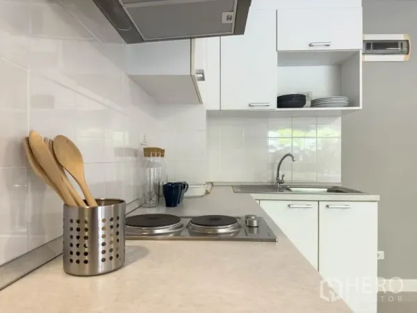 Condominium for sale in Watthana, Bangkok - Compact white kitchen with electric cooktop, hood, and utensils.