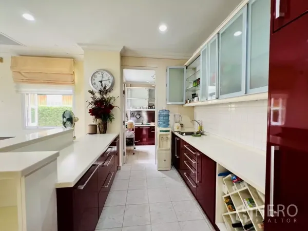 Detached House for rent in Prawet, Bangkok - Fitted kitchen with white countertops, glossy burgundy cabinets and a window.