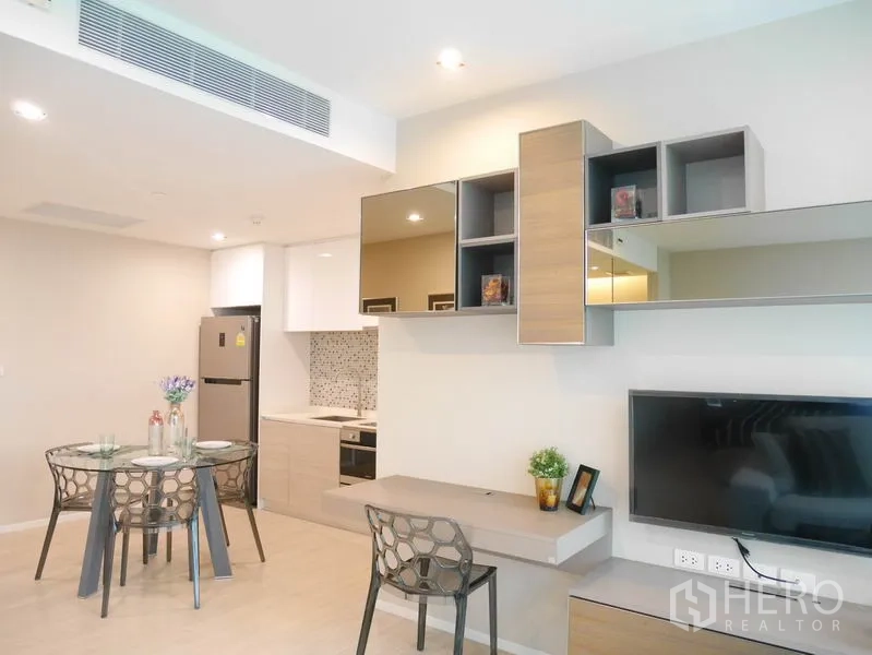 Condominium for rent or sale in Watthana, Bangkok - Open-plan living with wall-mounted TV, floating desk and modern kitchenette with mosaic backsplash.