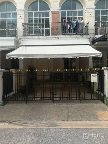 联排别墅 出售在Bang Kapi, Bangkok - 房屋正面，黑色金属栅栏与遮阳棚车库，楼上拱形落地窗。