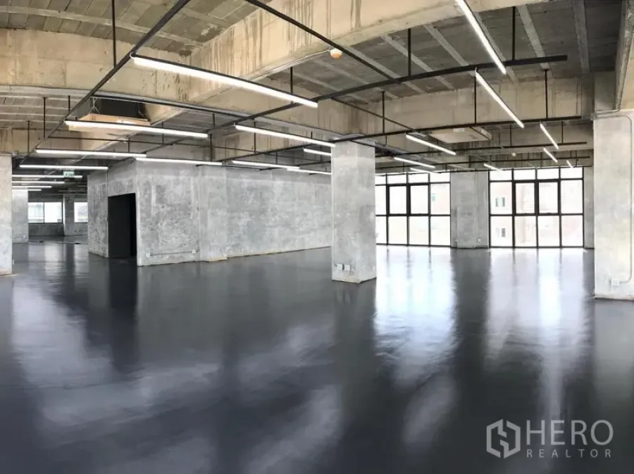 Office Space for rent in Khlong Toei, Bangkok - Spacious open-plan loft office with exposed concrete ceiling, linear LED lights, polished black floors, and large grid windows.