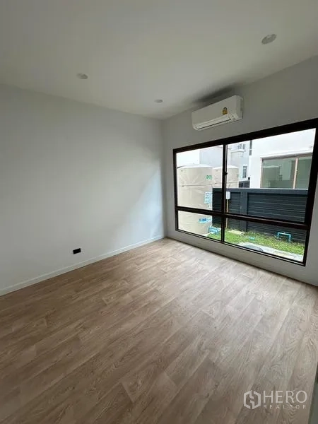 Detached House for rent in Bang Kapi, Bangkok - Bright bedroom with wood-look flooring, large window and wall-mounted air conditioner.